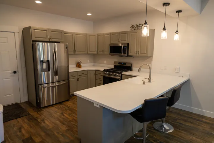 Modern kitchen featuring wood-finish flooring, stainless steel appliances, grey cabinetry, quartz countertops, and a peninsula with seating