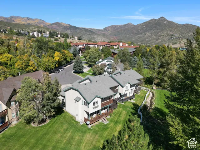 Mountain-backed property featuring a green shingle roof, private balconies, and a sloped grassy yard
