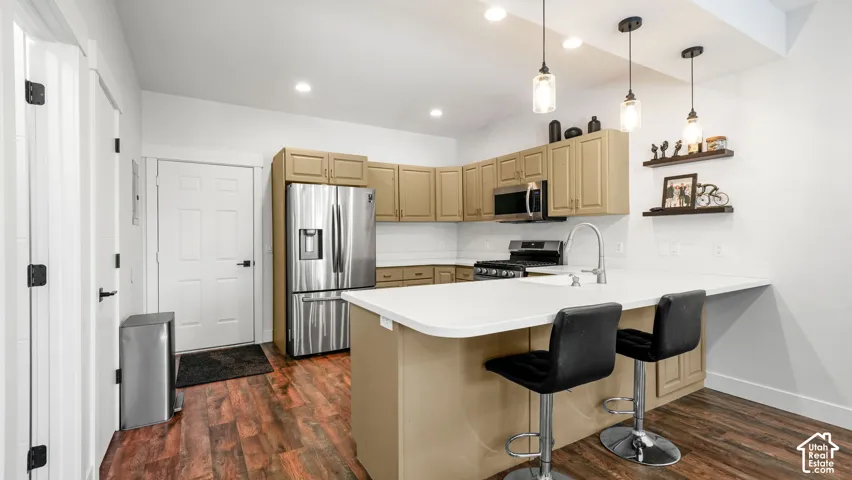 Kitchen featuring wood-finish flooring, stainless steel appliances, light-toned cabinetry, a spacious island with an integrated sink, and pendant lighting fixtures