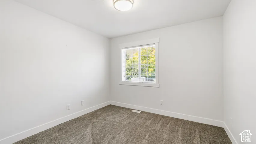 Bright interior space featuring neutral wall tones, window with horizontal blinds, and dark gray carpet
