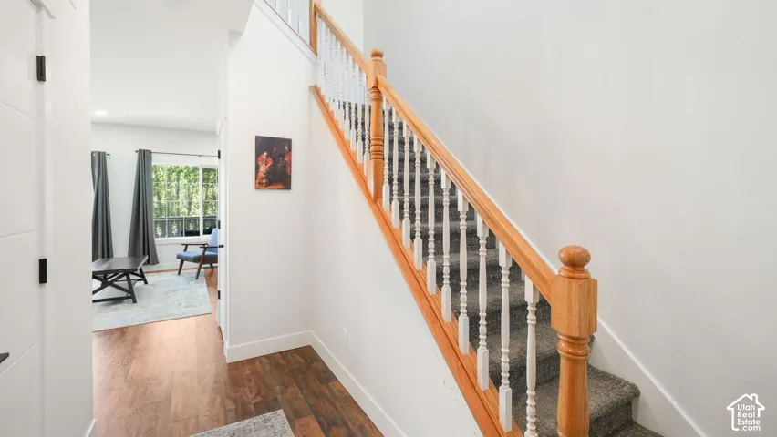 Wood-finish flooring leading to a carpeted staircase with a wood handrail and painted balusters, hall way to main living area