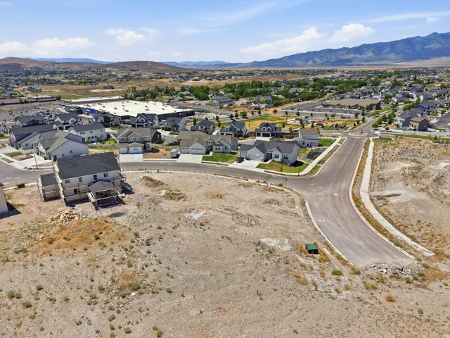 Newly developed residential neighborhood with paved streets and sidewalks, featuring a prominent, partially constructed home and distant mountain ranges