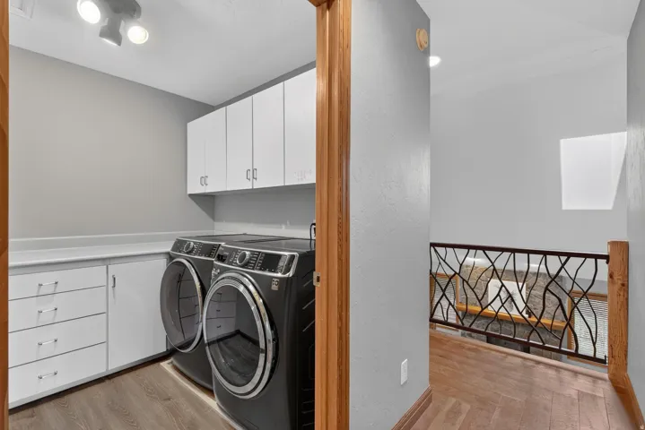 Dedicated laundry area featuring white cabinetry, integrated countertop space, and wood-finish flooring