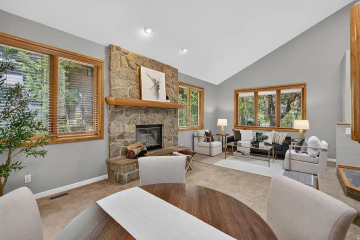 Living area featuring a stone fireplace with a wood mantel, vaulted ceilings, and natural wood-framed windows