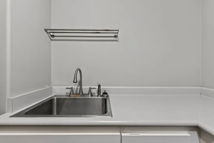 Stainless steel utility sink with a high-arc faucet, integrated into a white countertop