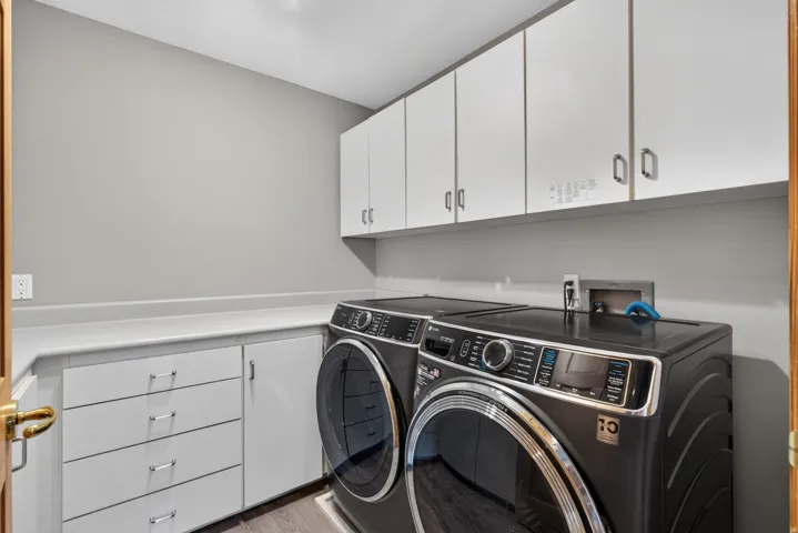 Laundry room featuring white cabinetry, a light-toned countertop, and wood-finish flooring