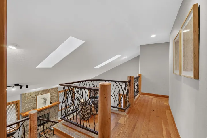 Upper-level hallway with wood-finish flooring, custom ironwork railing, and two skylights