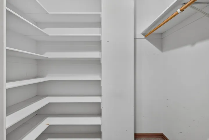 Walk-in closet featuring extensive built-in shelving, a garment rod, and wood-finish flooring