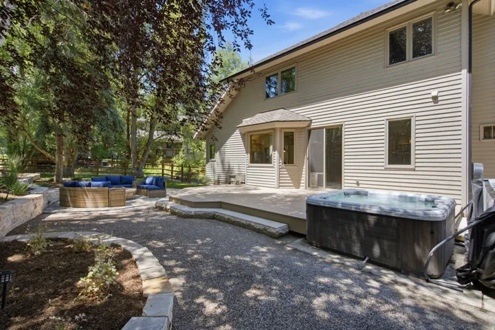 Rear exterior featuring a spacious composite deck, built-in spa, sliding glass door, bay window, and gravel patio area with stone retaining walls