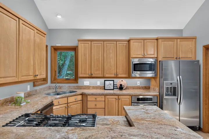 Kitchen featuring abundant wood cabinetry, integrated stainless steel appliances, granite countertops, a built-in gas range, and a double basin sink