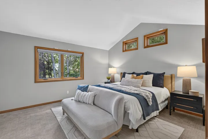 Vaulted ceiling bedroom featuring wood-trimmed windows, neutral wall tones, and carpeted flooring