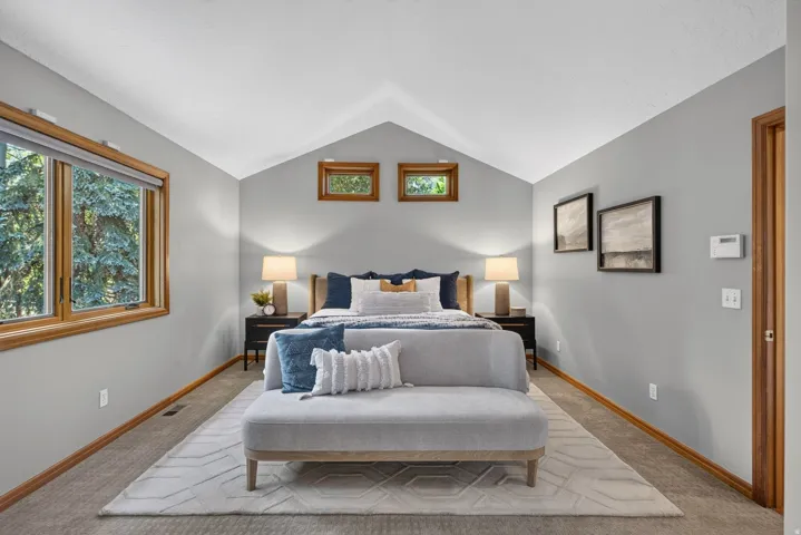 Bedroom featuring vaulted ceilings, wood-framed windows, and carpet flooring