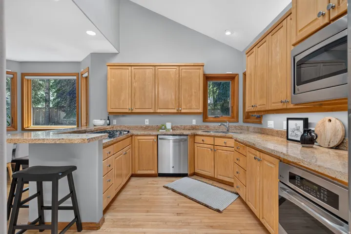 Kitchen featuring natural wood cabinetry, light-toned countertops, stainless steel appliances, and wood-finish flooring