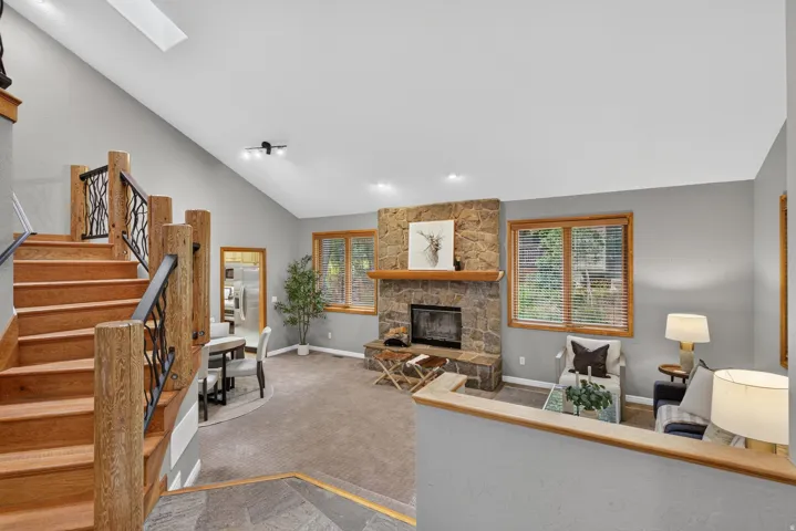 Vaulted ceilings complement an open living space featuring a stone-clad fireplace with a wood mantle