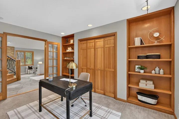 Carpeted room featuring natural wood bi-fold closet doors, built-in shelving, and French doors opening to an adjacent flagstone floor