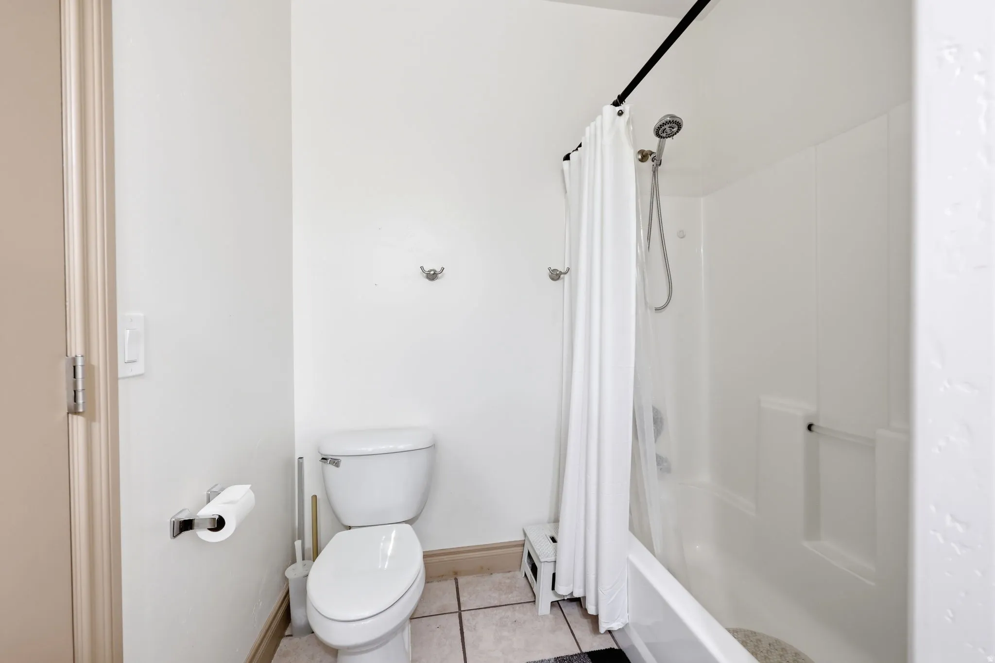 White-tiled bathroom featuring a standard toilet, a tub-shower combination with a curtain rod, and wall-mounted towel hooks