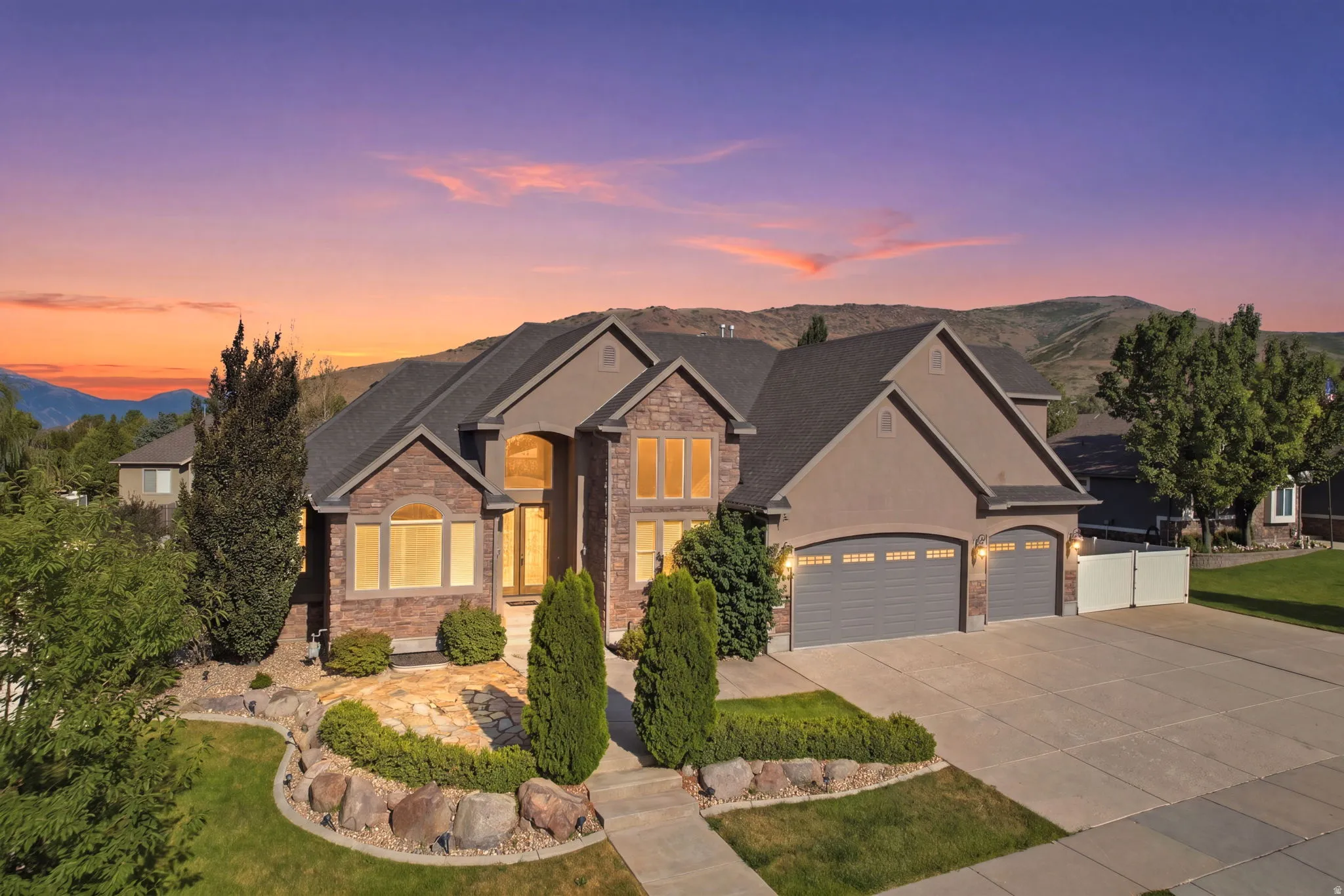 Stately multi-level residence featuring stone and stucco exterior, a prominent three-car garage, and a concrete driveway