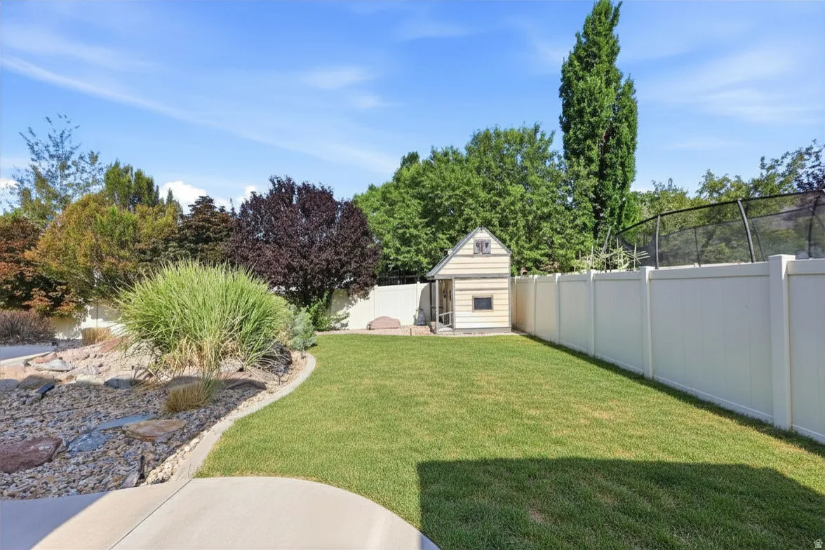 Expansive backyard featuring a manicured lawn, a detached storage shed, a white privacy fence, and mature landscaping with decorative rock beds