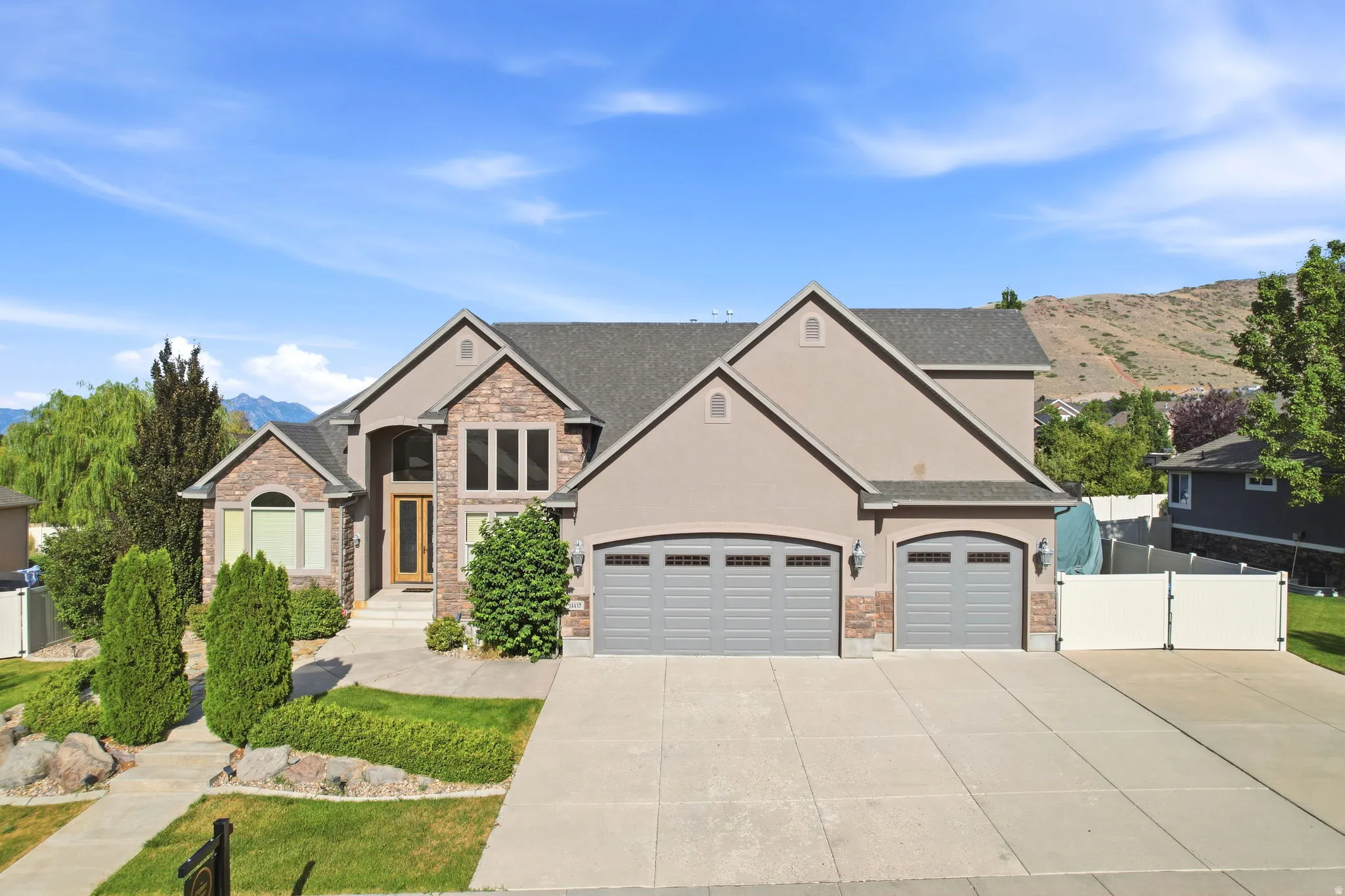 Stucco exterior featuring stone accents, a multi-car driveway, arched garage doors, and mature landscaping