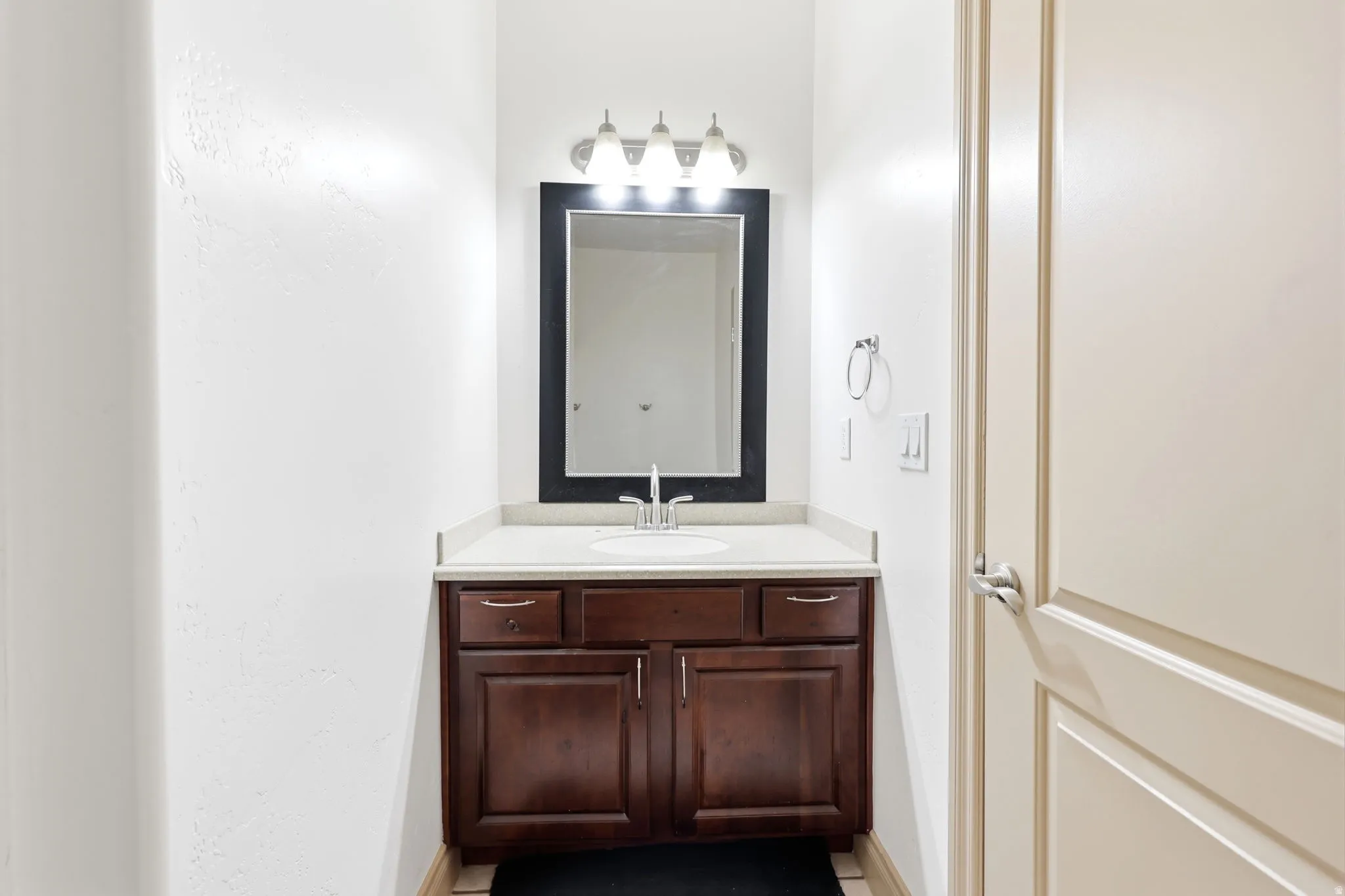 Bathroom vanity featuring a dark wood-finish cabinet, a light-toned countertop with integrated sink, and a framed mirror with overhead lighting