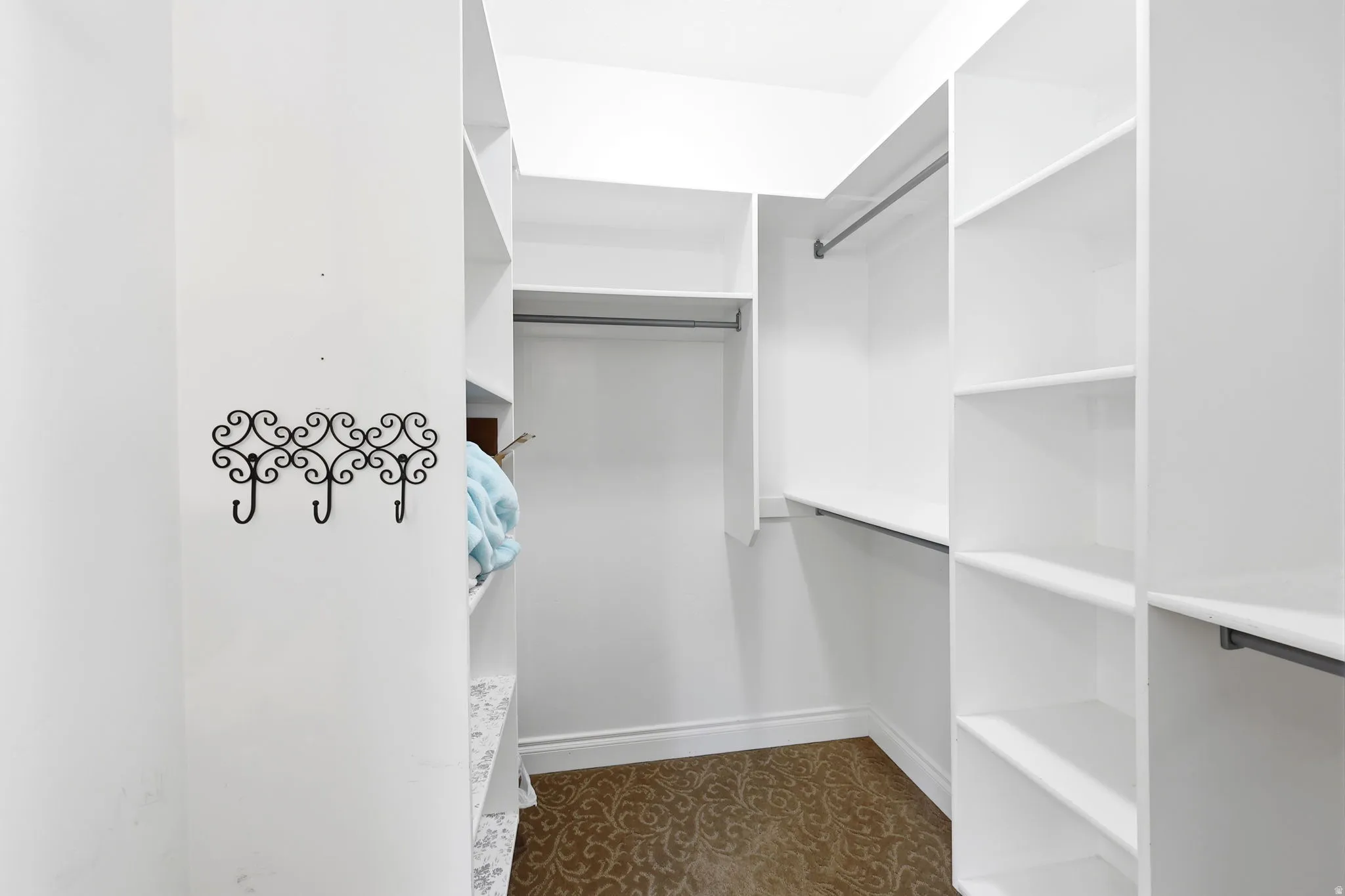 Walk-in closet featuring white built-in shelving, multiple hanging rods, and patterned flooring