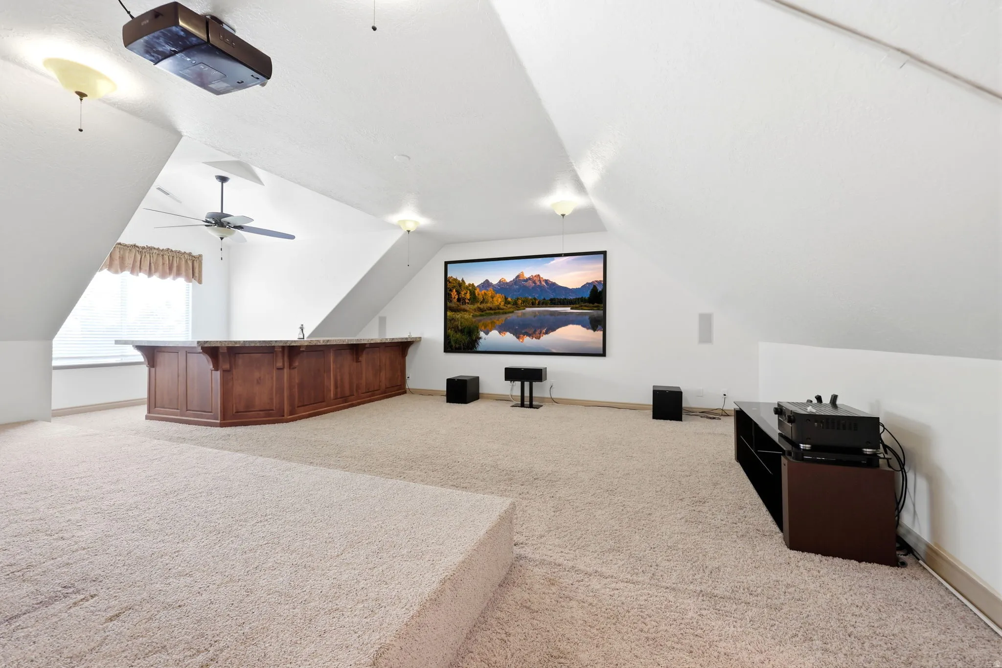 Spacious bonus room featuring a large projection screen, built-in wooden bar with countertop, and plush carpeted flooring