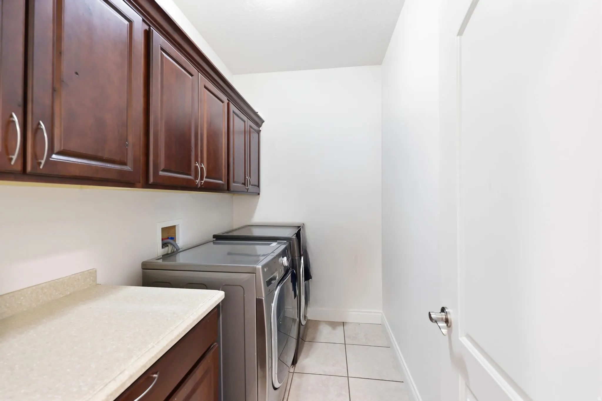 Laundry room featuring extensive dark wood cabinetry, a light-toned countertop, and light-colored tile flooring