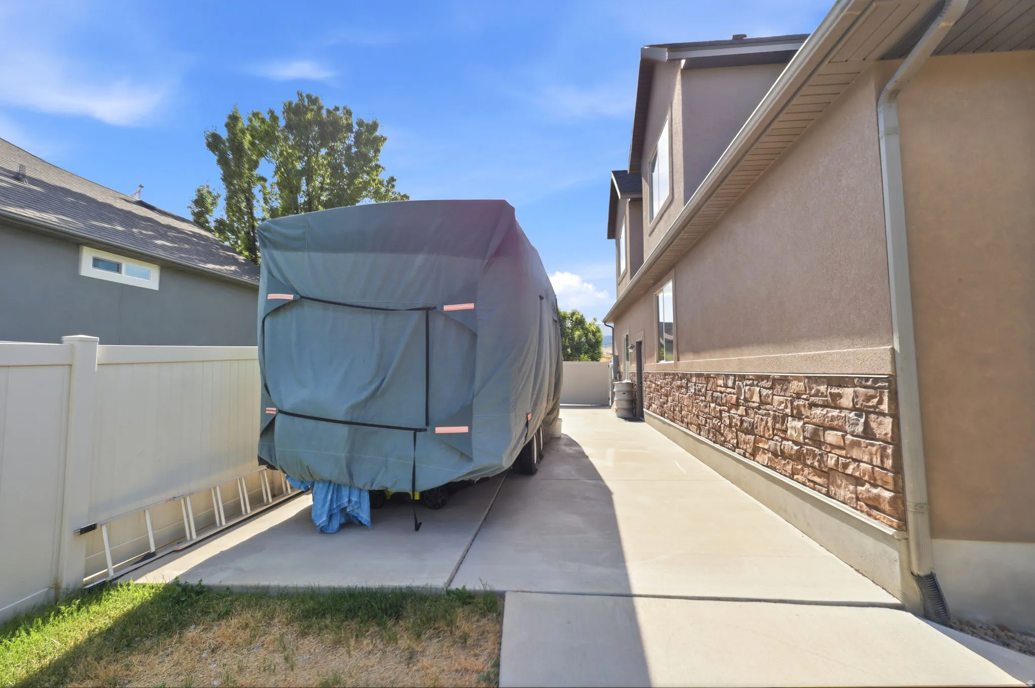Paved side access with concrete pathway, vinyl fencing, and a stone facade accenting the exterior