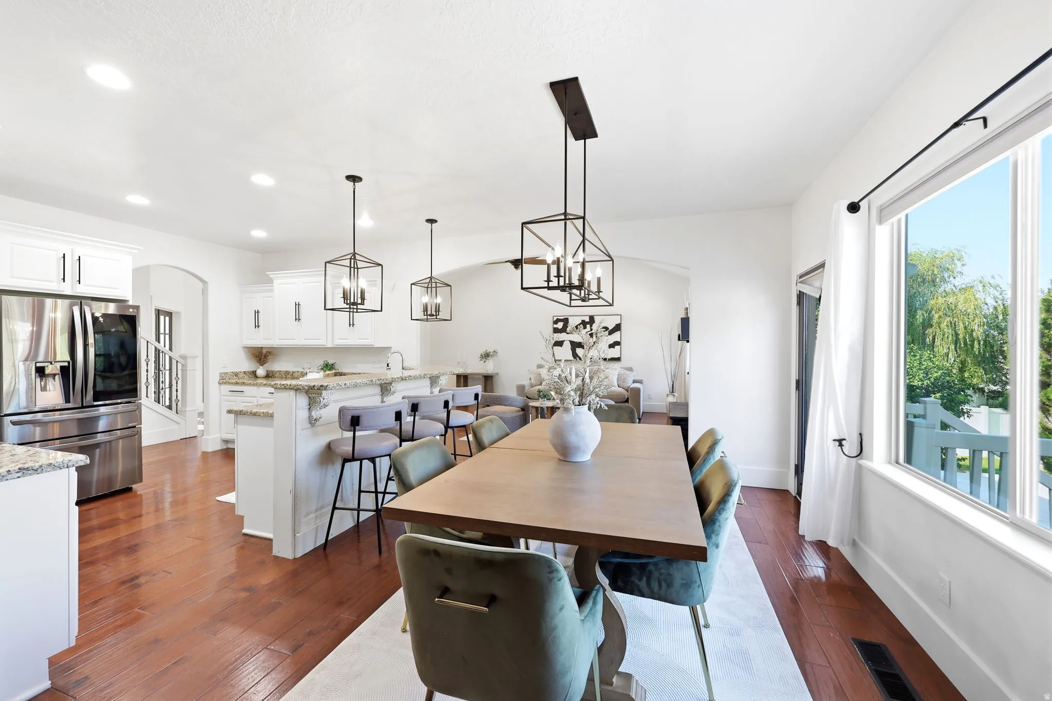 Open-concept living space featuring wood-finish flooring, white cabinetry, granite countertops, and black geometric pendant lighting