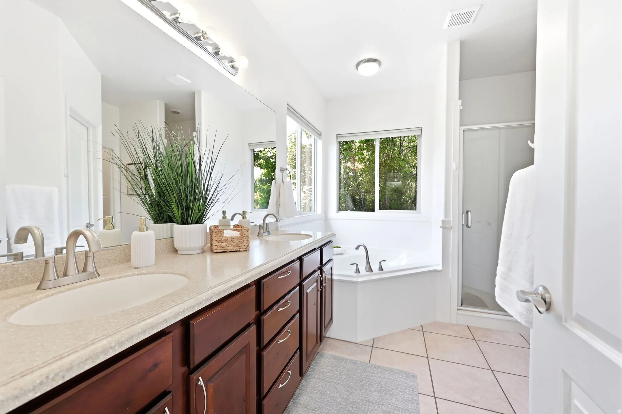 Bathroom featuring a dual vanity with a light-colored countertop, rich wood-finish cabinetry, a large built-in mirror, a corner soaking tub, and a separate glass-enclosed shower