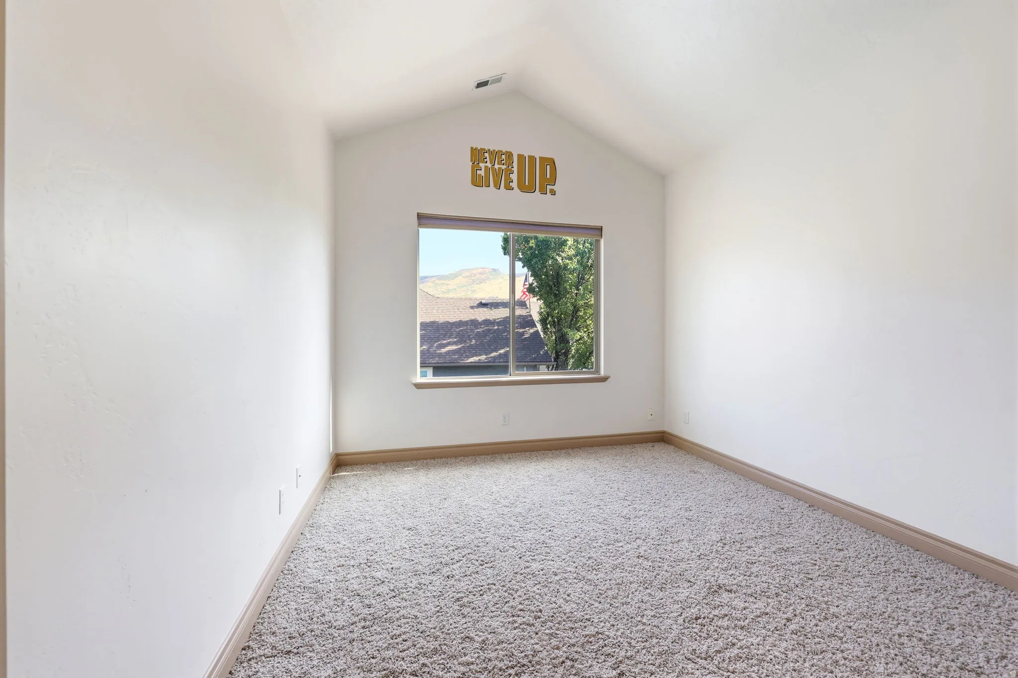 Bright room featuring vaulted ceilings, a large window with natural wood-finish trim, beige wall-to-wall carpeting, and white painted walls