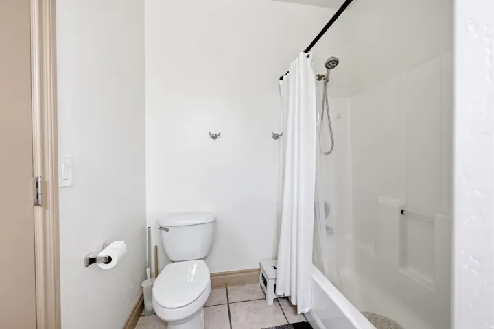 White-tiled bathroom featuring a standard toilet, a tub-shower combination with a curtain rod, and wall-mounted towel hooks