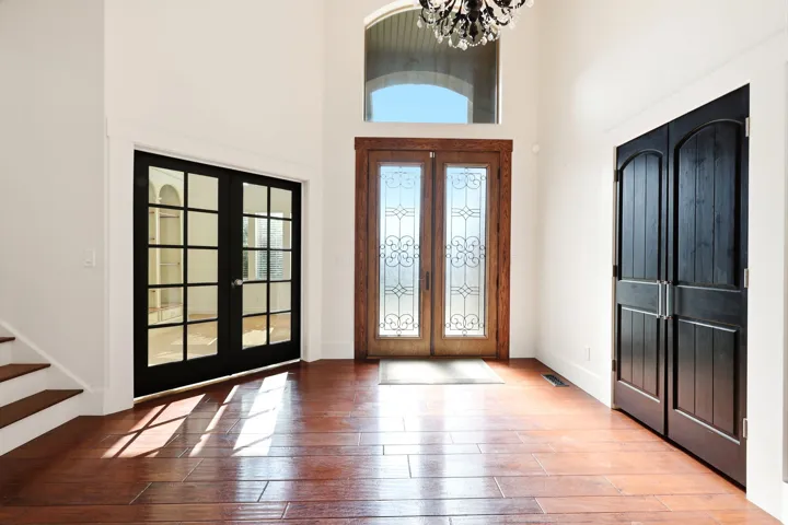 Grand entryway featuring wood-finish flooring, a double-door entry with decorative glass inserts and an arched transom window, a crystal chandelier, and black French doors