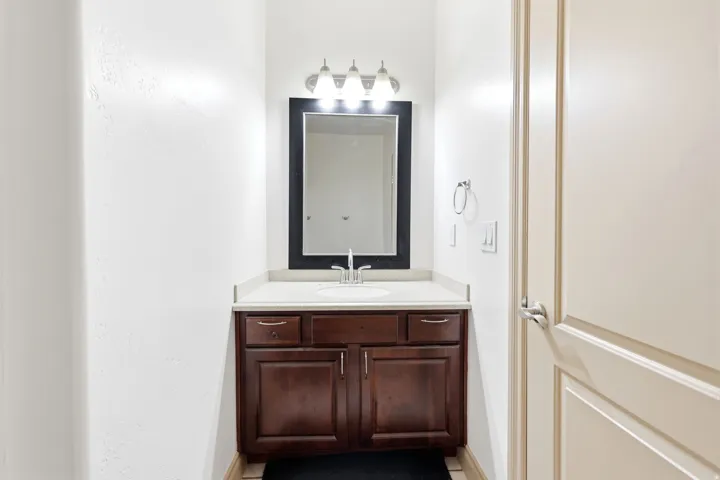 Bathroom vanity featuring a dark wood-finish cabinet, a light-toned countertop with integrated sink, and a framed mirror with overhead lighting