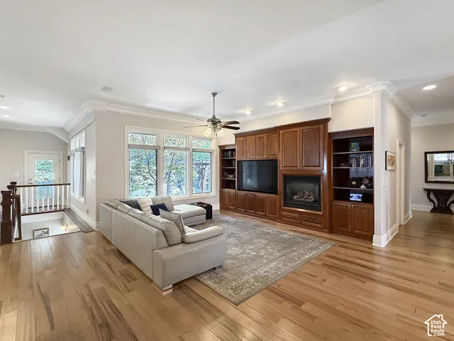 Spacious living room with built in shelves, crown molding, hardwood floors, and ceiling fan.
