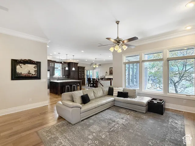 Spacious living room with built in shelves, crown molding, hardwood floors, and ceiling fan.