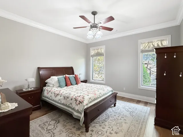 Primary bedroom with crown molding, hardwood flooring and ceiling fan.
