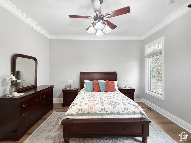 Primary bedroom with crown molding, hardwood flooring and ceiling fan.