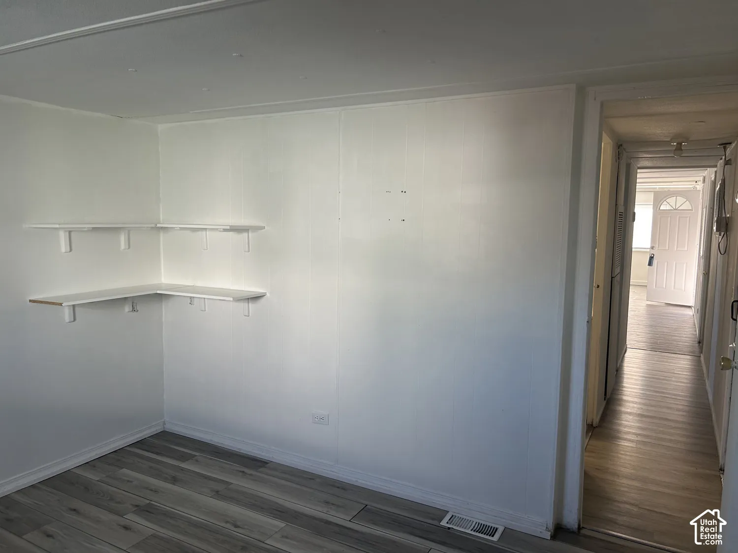 Room featuring wood-finish flooring, white panel walls, and built-in corner shelving