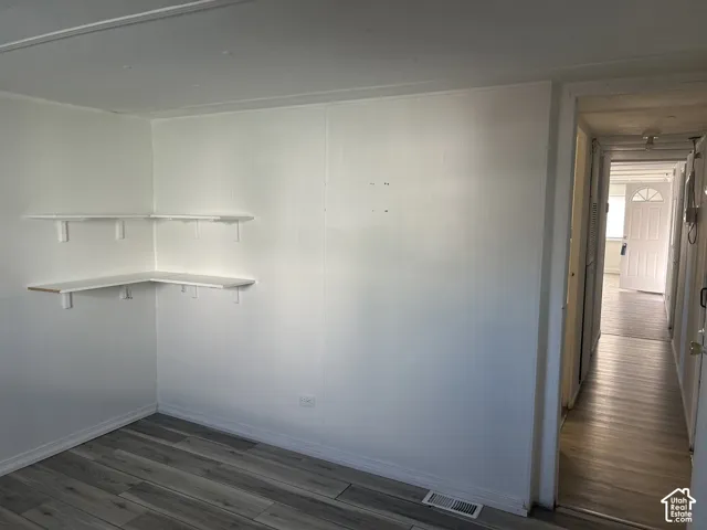 Room featuring wood-finish flooring, white panel walls, and built-in corner shelving