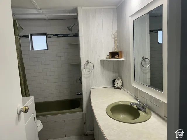 Bathroom featuring a tub/shower combination, white subway tile surround with accent band, and a vanity with an integrated sink. Washer and Dryer. Storage shelf.