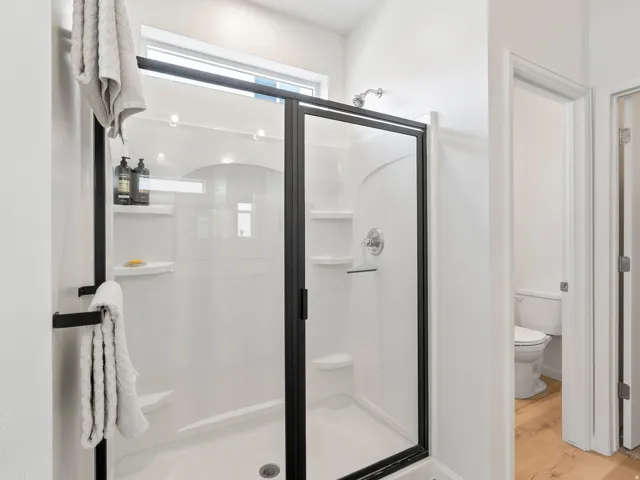 Bathroom featuring a shower enclosure with a dark-framed glass door, white shower surround with built-in shelving, chrome shower fixtures, and a transom window