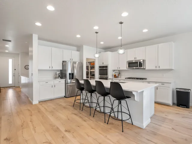 Contemporary kitchen featuring an expansive center island with seating, white shaker cabinetry, stainless steel appliances, recessed lighting, and wood-finish flooring