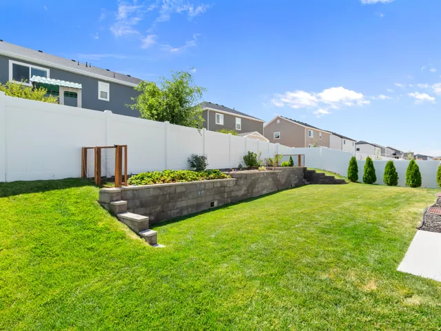 Expansive rear yard featuring a tiered layout with lush green lawn, a stone retaining wall, and a dedicated garden bed