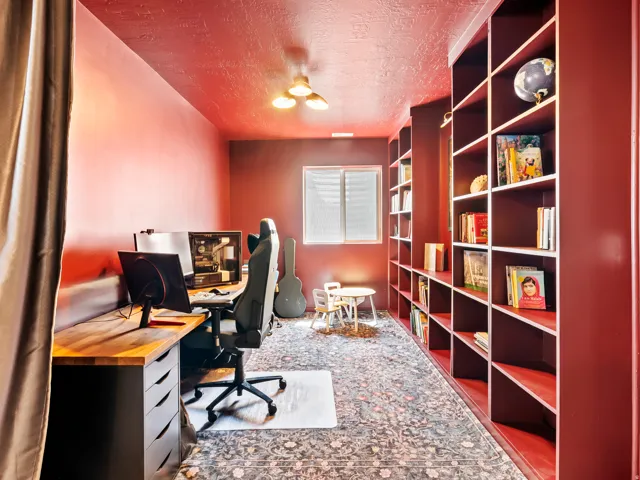 Dedicated room featuring extensive built-in shelving, a built-in desk with wood-finish top, and a window with blinds