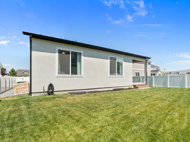 Expansive backyard featuring a manicured lawn, white vinyl fencing, stucco exterior, and a wooden deck with steps