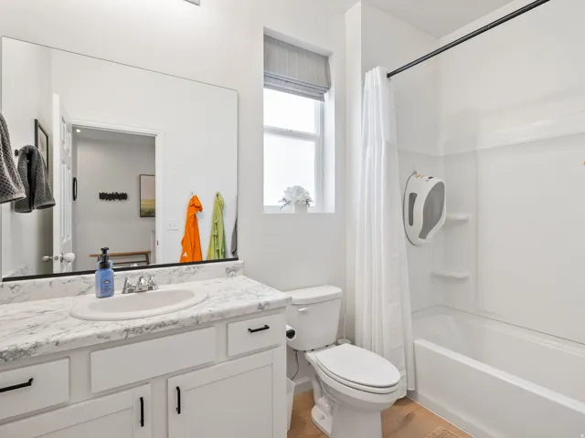 Bathroom featuring a vanity with a white countertop and undermount sink, white cabinetry with black hardware, a shower-tub combination with a white surround, and light wood-finish flooring