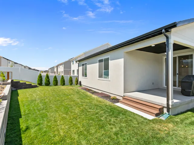 Expansive backyard featuring a manicured lawn, tiered landscaping with retaining walls, and a row of evergreen shrubs