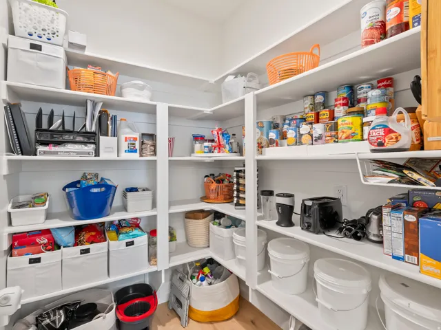 Spacious walk-in pantry featuring extensive built-in shelving, white shiplap walls, light wood-finish flooring, and multiple electrical outlets