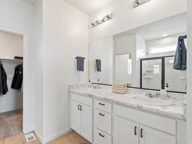 Double vanity with white cabinetry and dark hardware, set against wood-finish flooring
